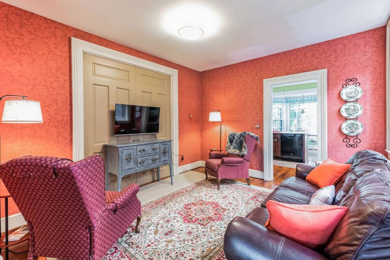 A living room with a TV, a red patterned armchair, a leather sofa, and a patterned rug.