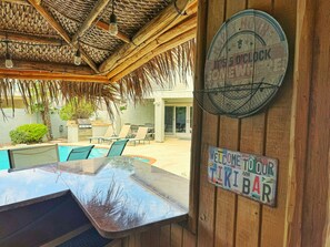 A poolside area with a wooden pergola, lounge chairs, and a bar area with a welcome sign.
