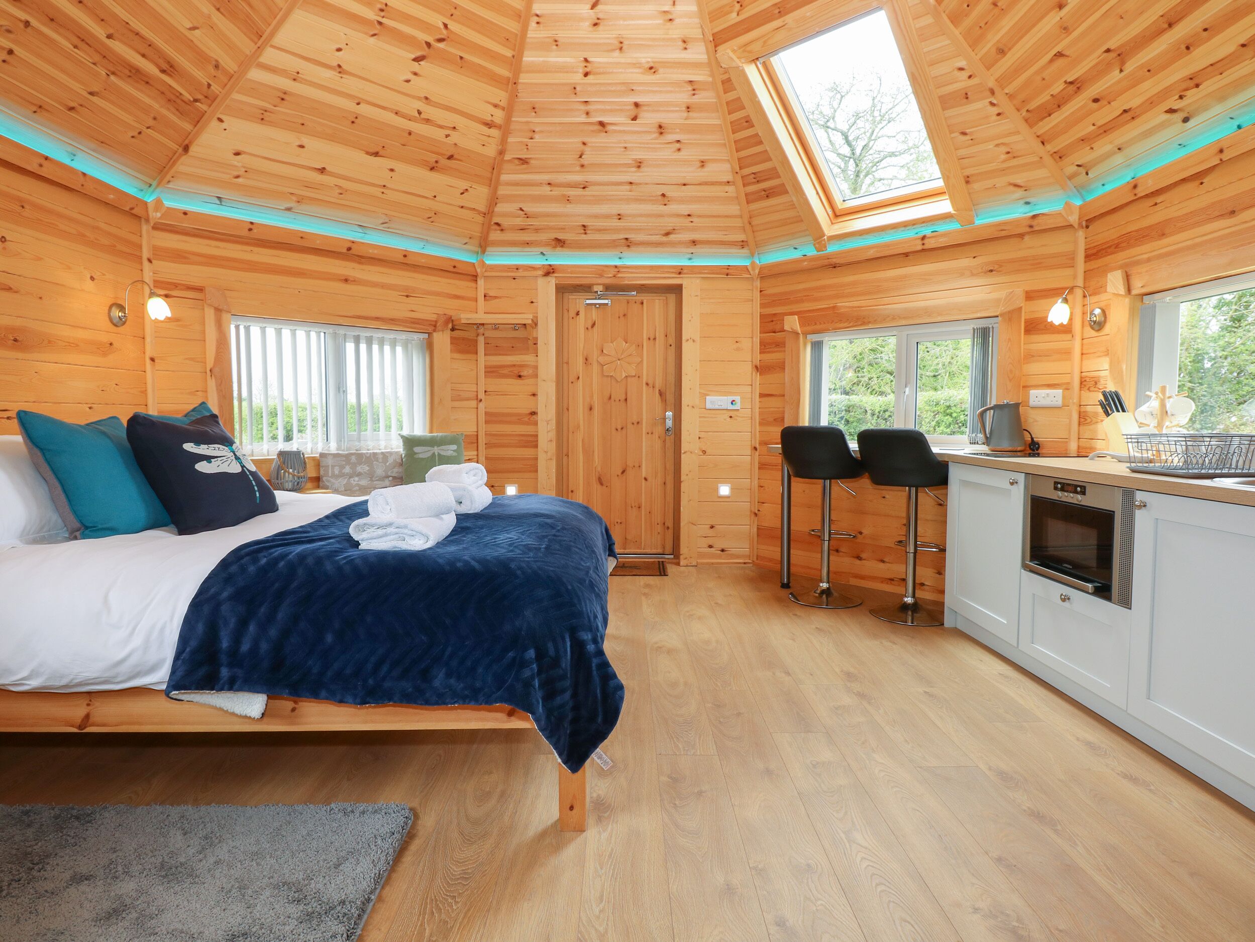 A wooden cabin interior with a bed, a small kitchenette, and a dining area.