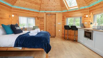 A wooden cabin interior with a bed, a small kitchenette, and a dining area.