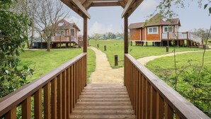 Een houten terras leidt naar een woongebied met huizen en een grasveld.