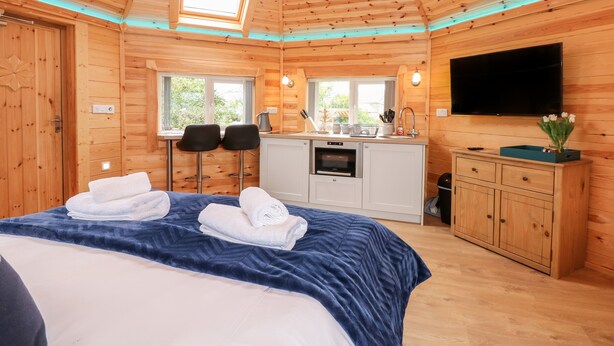 Een knus houten huisje met een bed, twee stoelen, een keuken en een televisie.