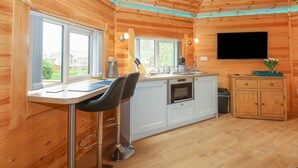 Een houten blokhut vanbinnen met een keuken, eethoek en een aan de muur bevestigde televisie.