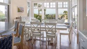 A dining area with a round table and chairs, large windows with a view of the ocean, and a ceiling fan. - 34 Surf Scoter at The Sea Pines Resort (Hilton Head Island)