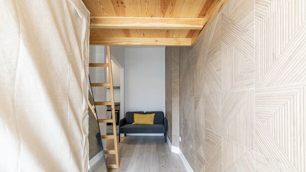 A narrow hallway with a wooden ceiling, a sofa with a yellow pillow, and a wooden ladder against the wall. - Charming Studio Located in the Heart of Lisbon (Lisboa)