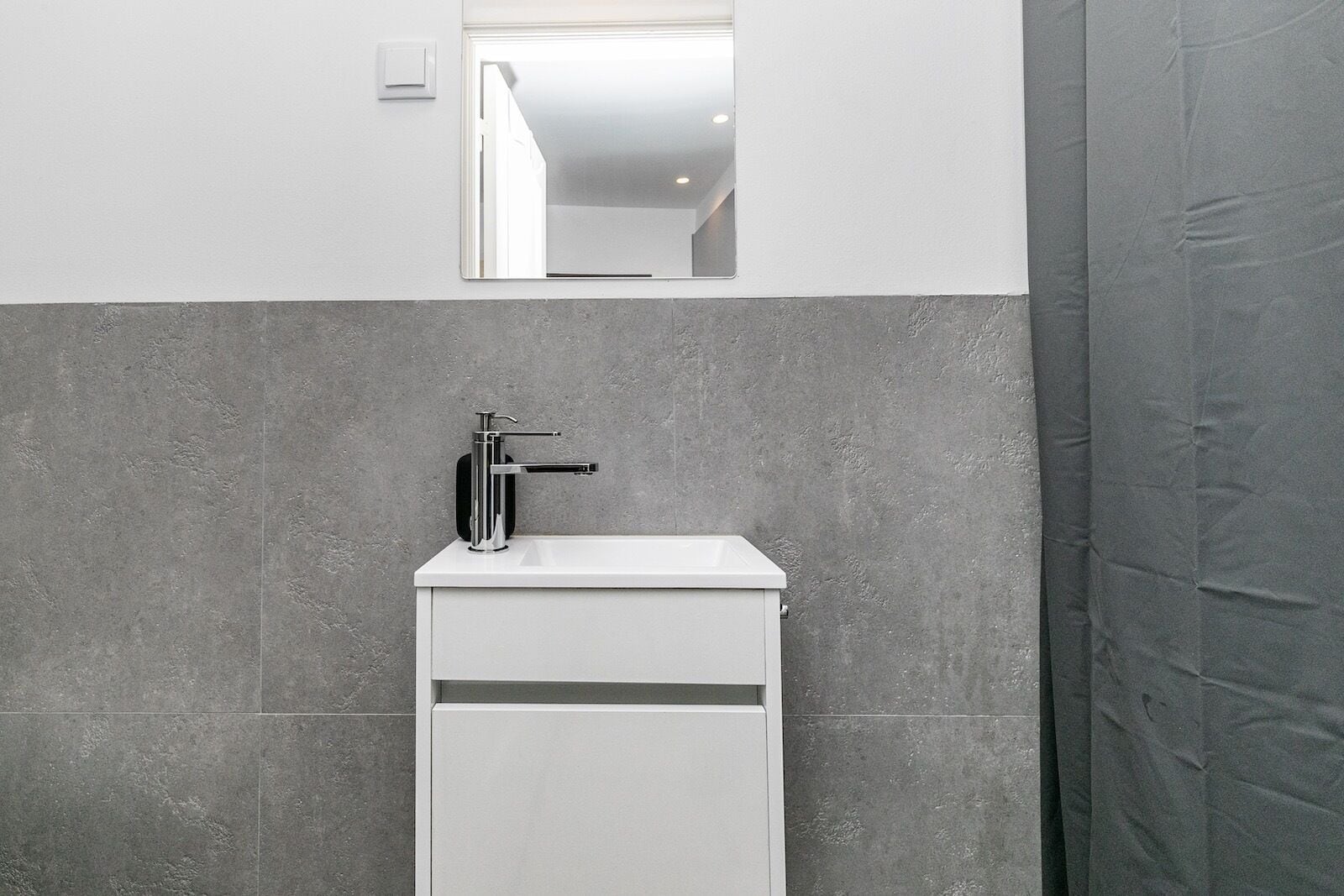 A bathroom with a white sink, a chrome faucet, and a mirror above it.
