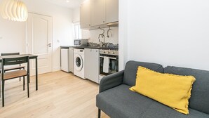 A compact living space with a dining area, a washing machine, an oven, and a sofa with a yellow cushion. - Charming Studio Located in the Heart of Lisbon (Lisboa)