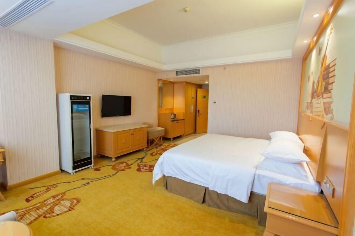 A hotel room with a bed, a wardrobe, a desk, a television, and a refrigerator.