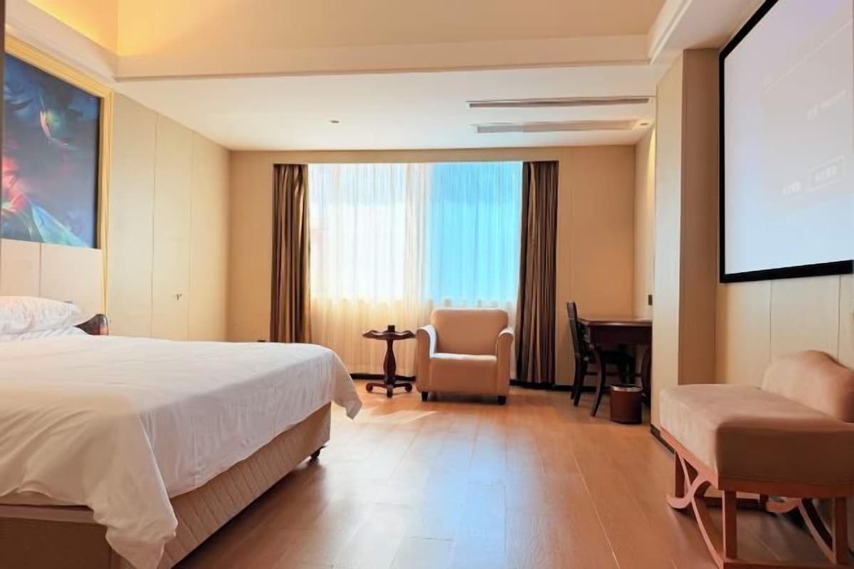 A hotel room with a bed, two armchairs, a small table, and a projector screen.