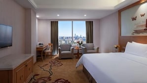 A hotel room with a large bed, a desk, two armchairs, a TV, and a view of the city skyline. - Victoria International Hotel (Kaiping Passenger Transport Terminal & Yihua Plaza Branch, Jiangmen) (Kaiping)