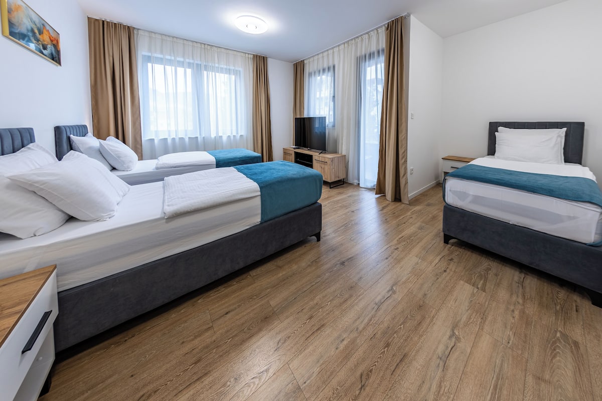 A hotel room with two beds, a TV, a wooden floor, and a window with curtains.