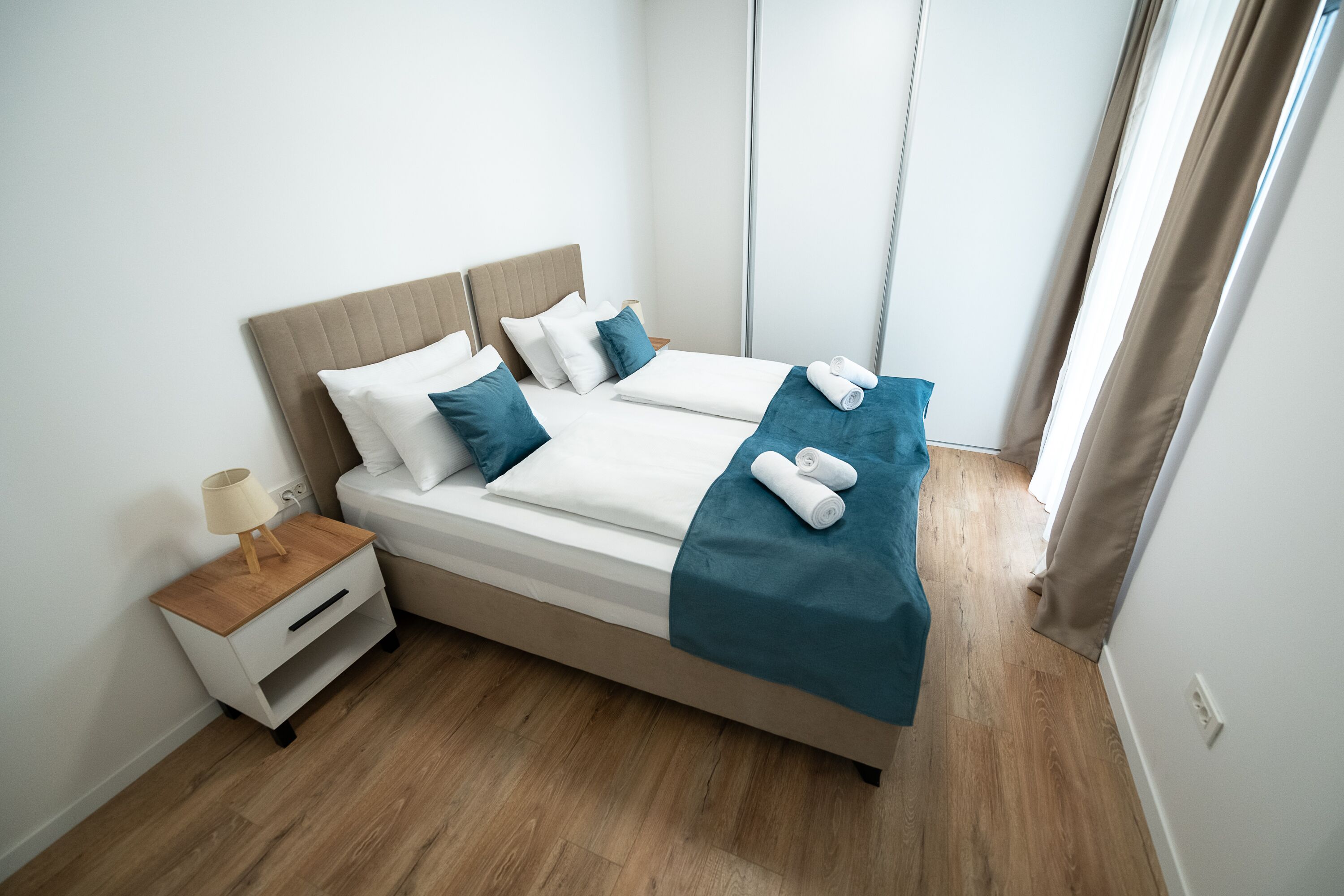 A neatly made twin bed with a wooden headboard, a nightstand with a lamp, and a blue blanket.