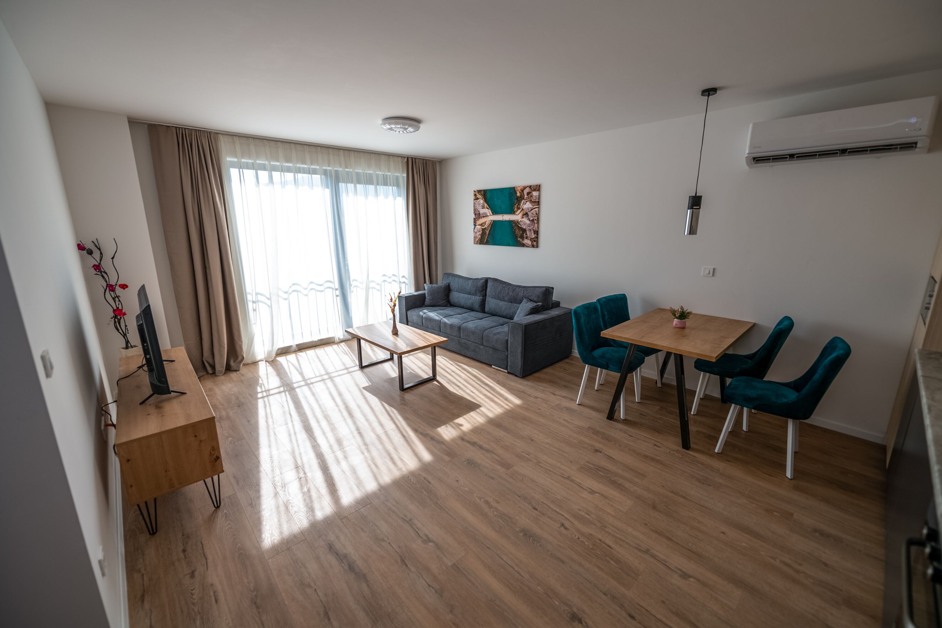 Un salon moderne avec un canapé gris, des fauteuils turquoise, une table basse en bois et un tableau accroché au mur.