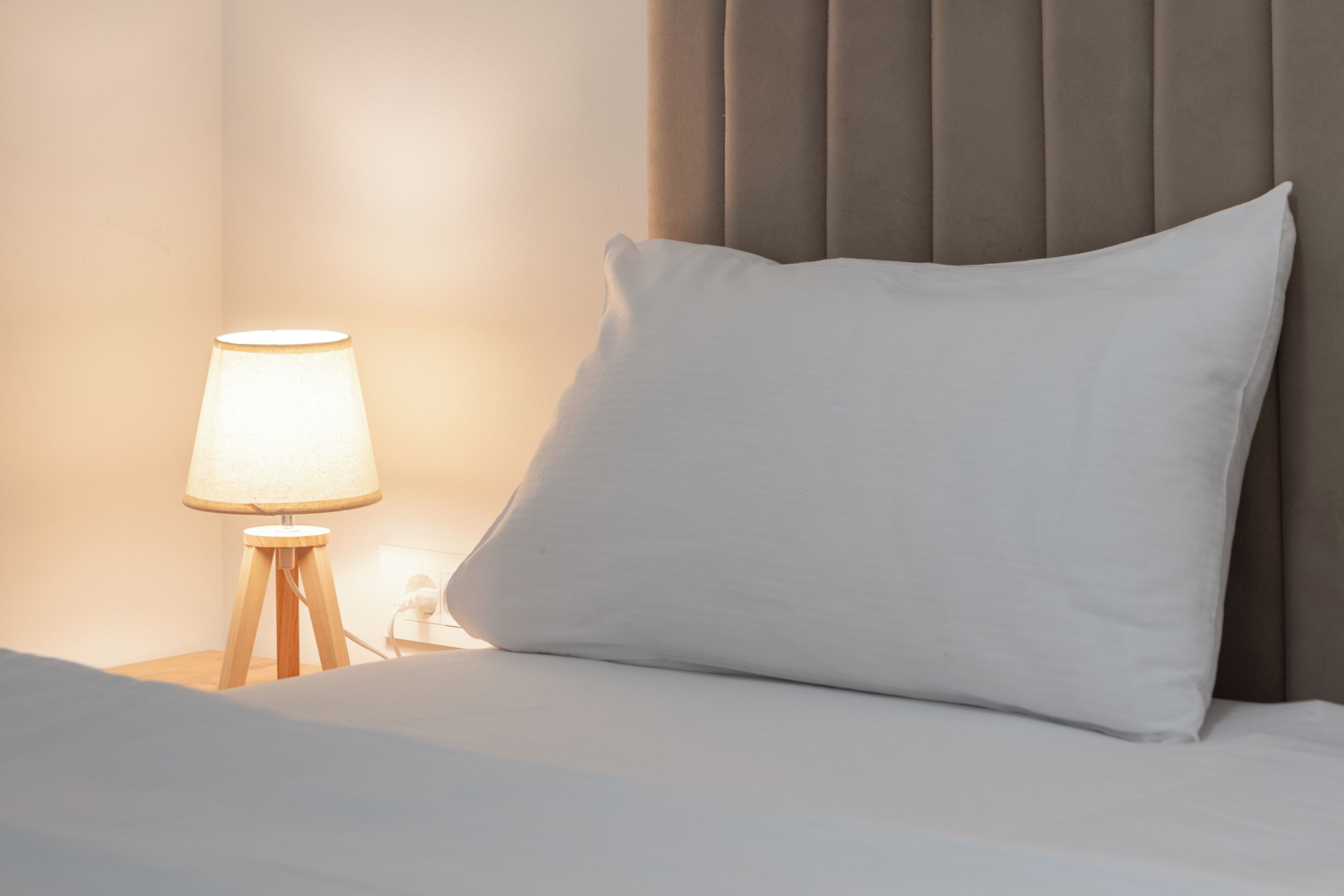 A bed with a white pillow and a bedside lamp on a wooden nightstand.