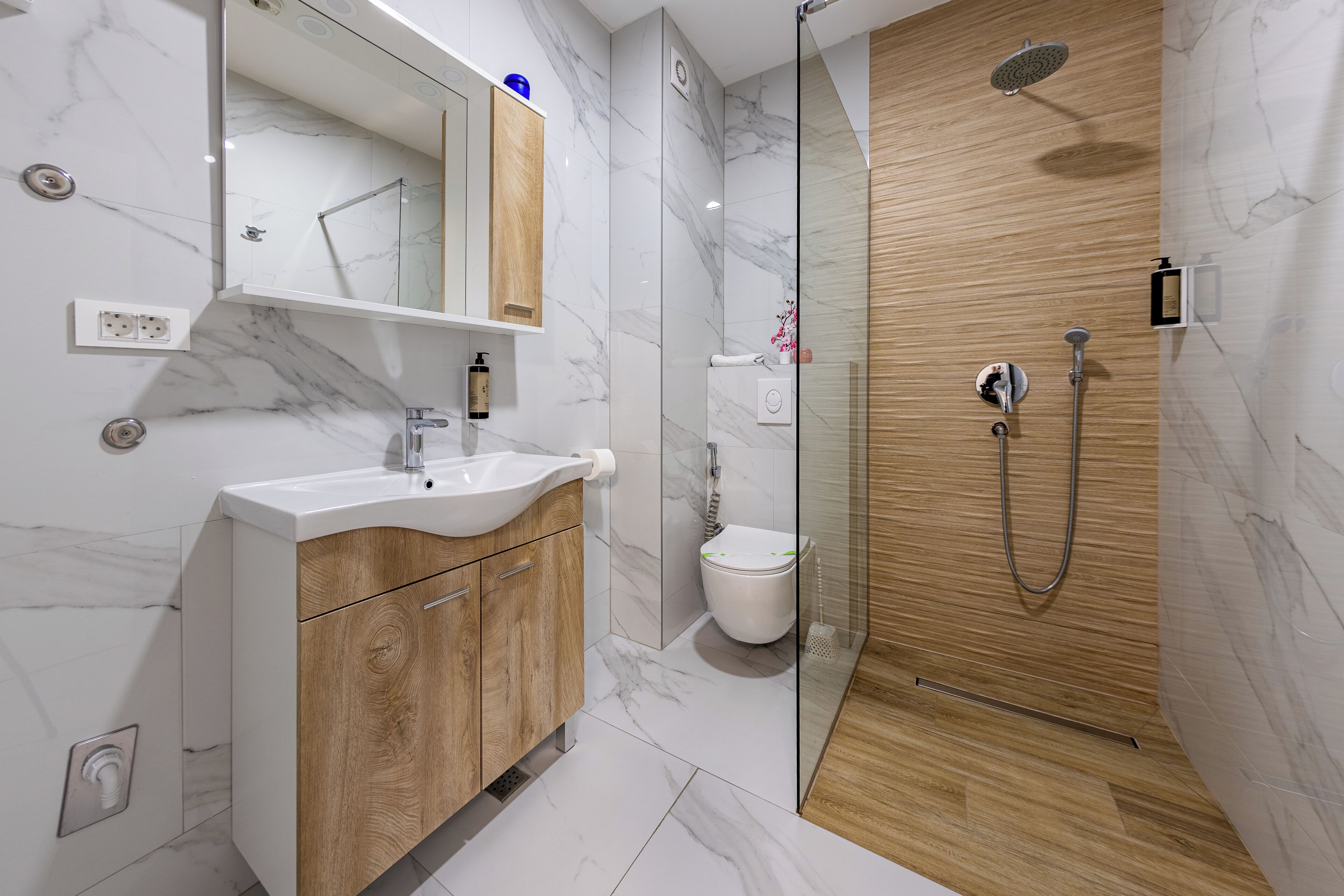 A modern bathroom with a marble sink, wooden cabinets, a glass shower enclosure, and a toilet.