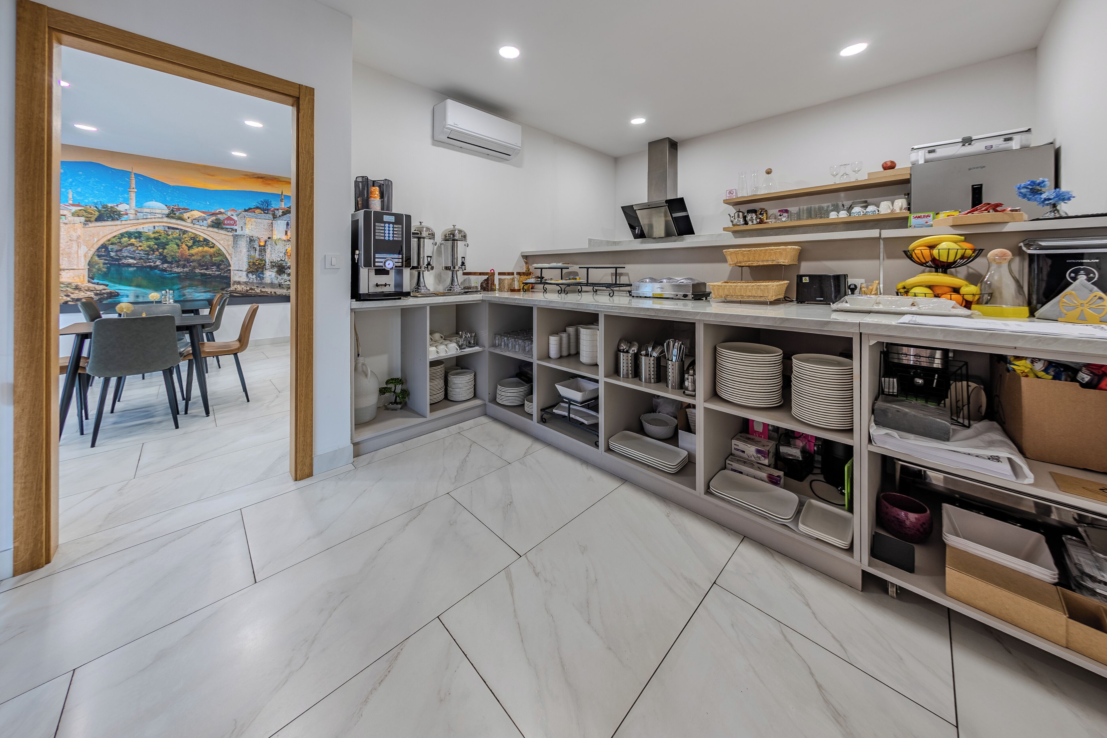 A modern kitchen with white marble floors, a dining area with chairs, and shelves with kitchenware.