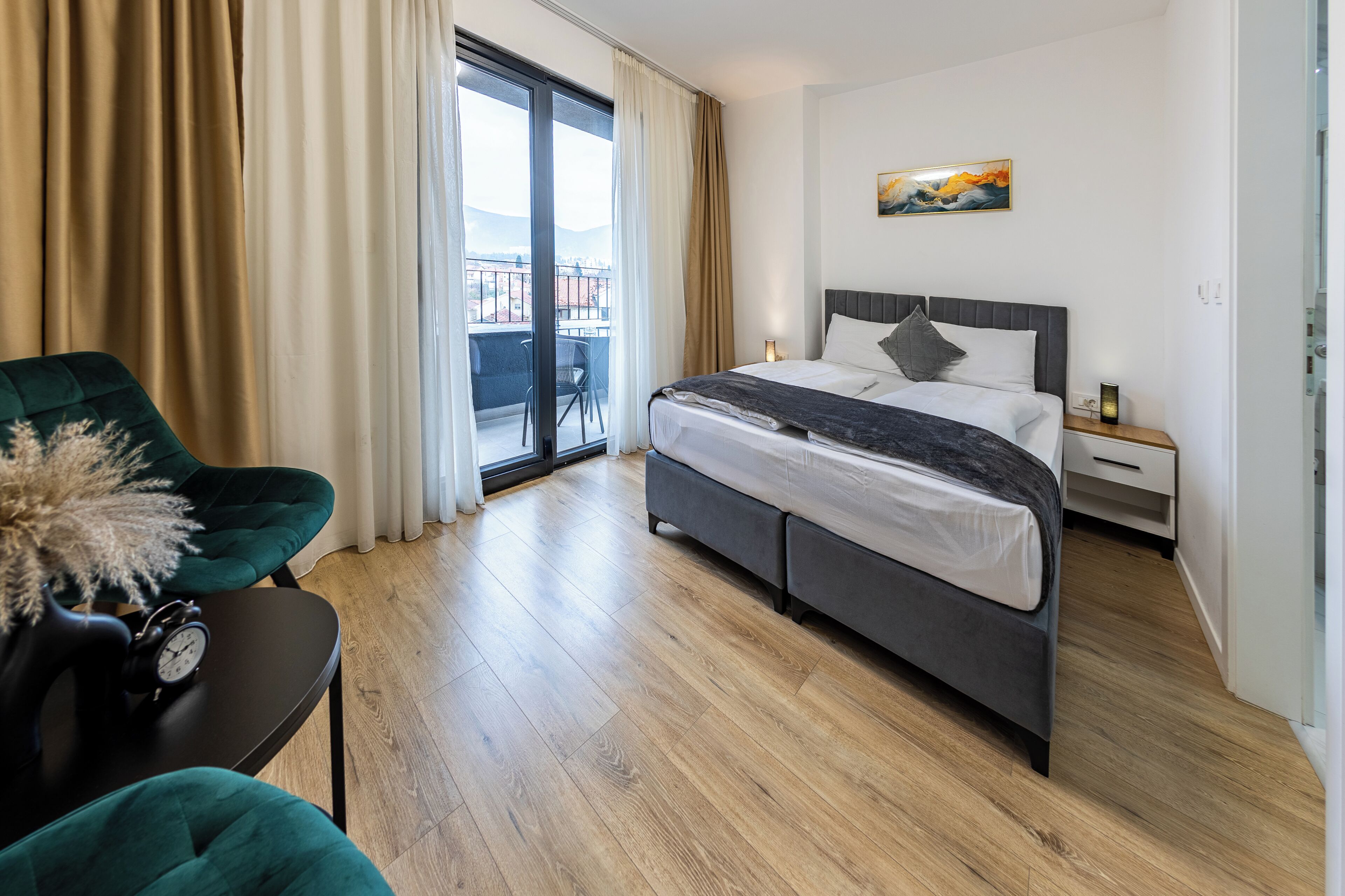 Hotellihuone, jossa on sänky, tuoli, pöytä, jossa on kello, yöpöytä ja taulu seinällä.