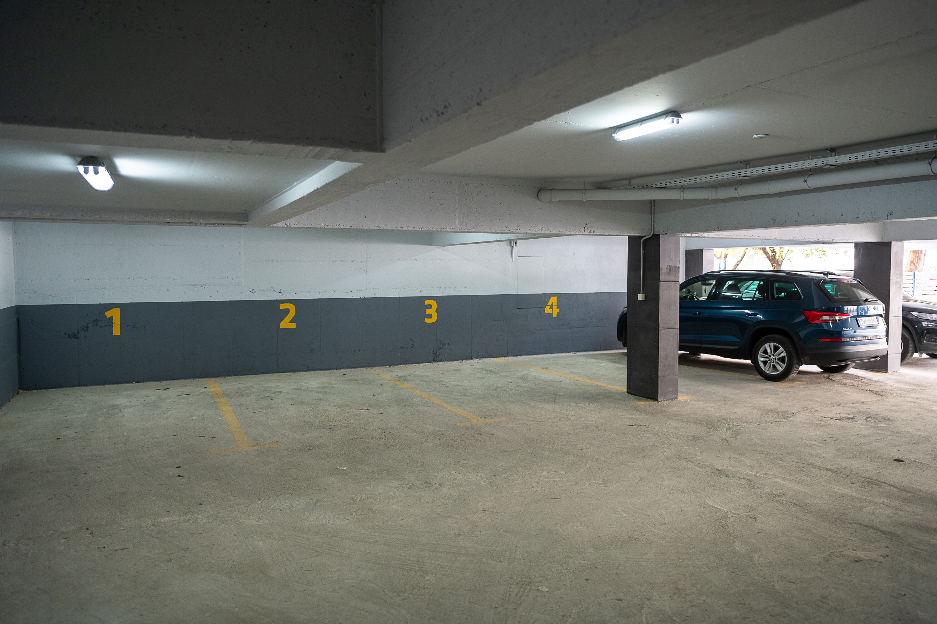 Un aparcamiento con plazas numeradas y un coche azul estacionado en la plaza número 4.