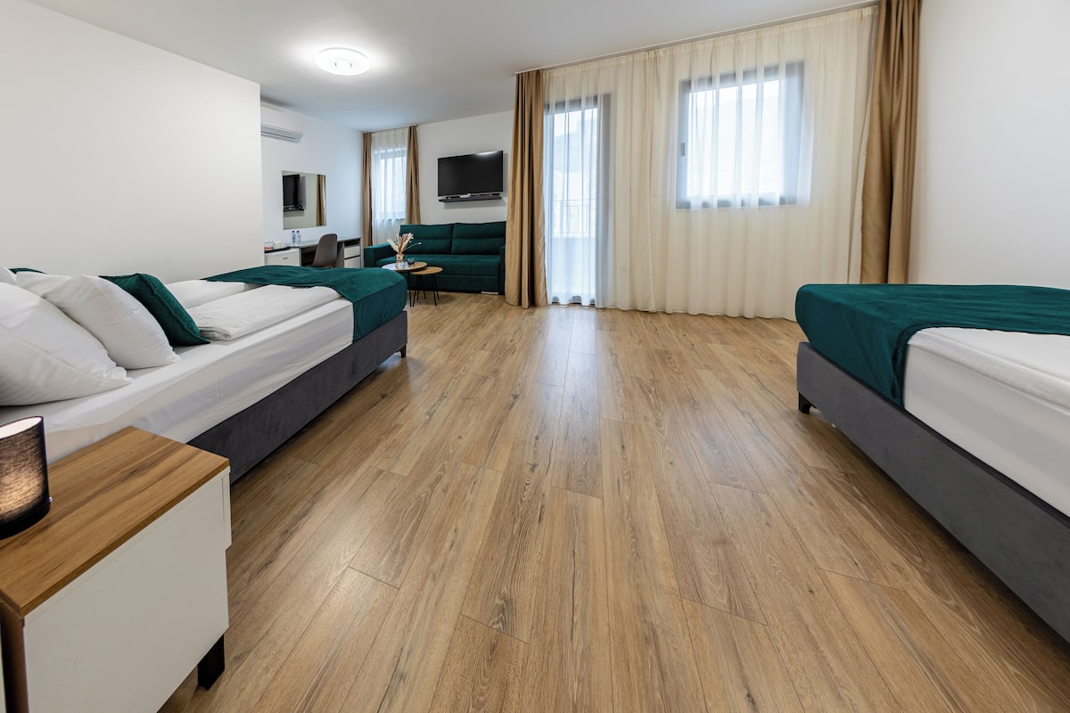 A hotel room with two beds, a desk, a chair, a TV, and a large window with curtains.