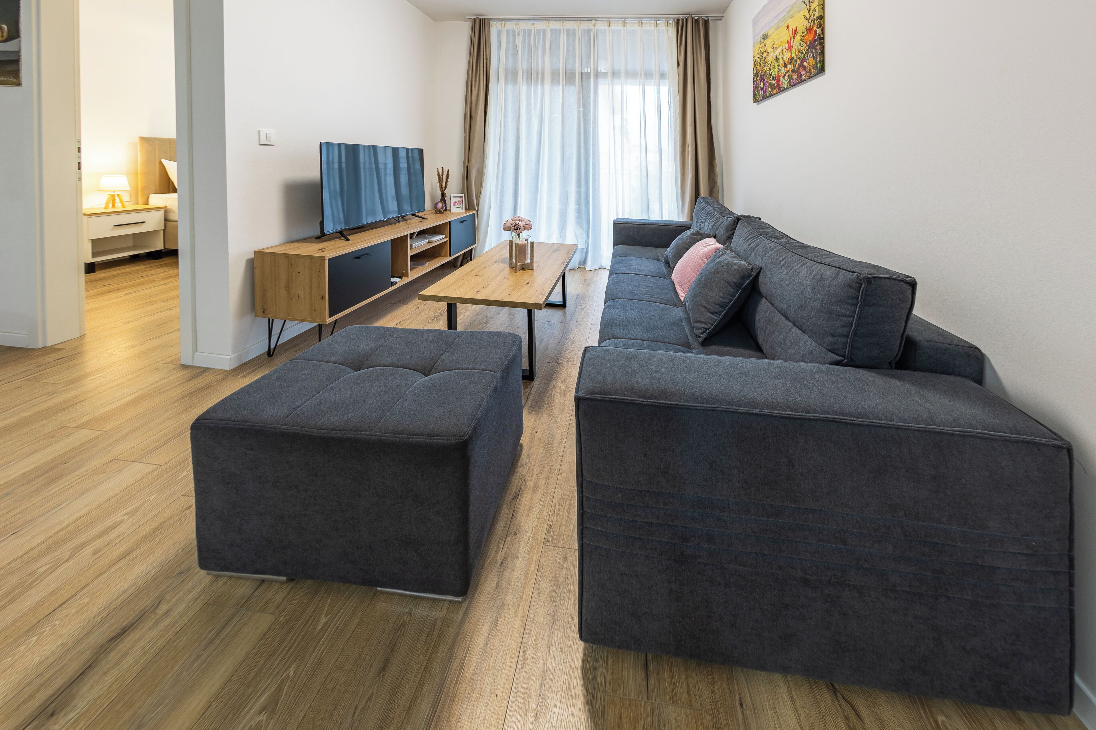 A modern living room with a grey sofa, ottoman, and a wooden coffee table.