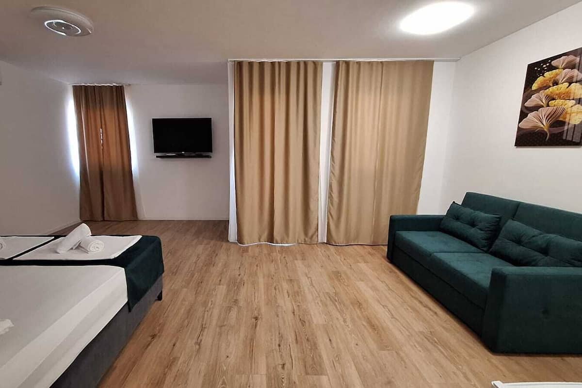 A hotel room with a bed, a green sofa, a flat-screen TV, and a window with curtains.