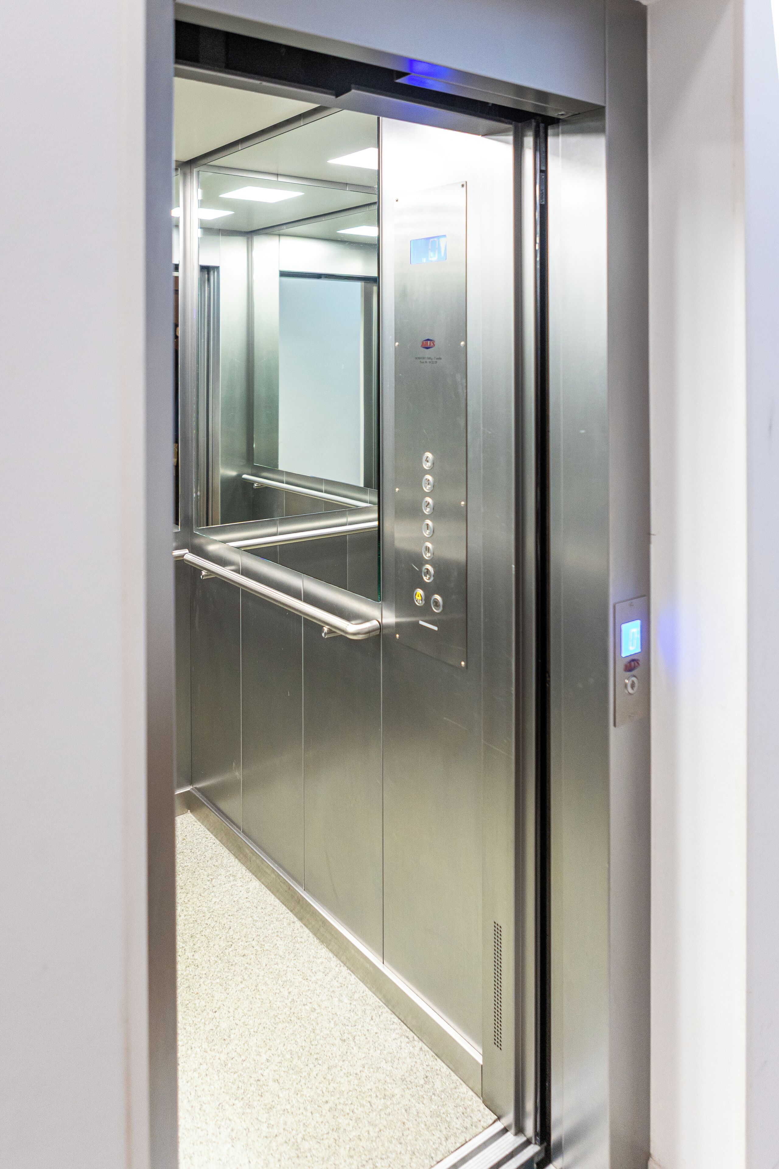 An elevator with metallic walls, a handrail, and a control panel.