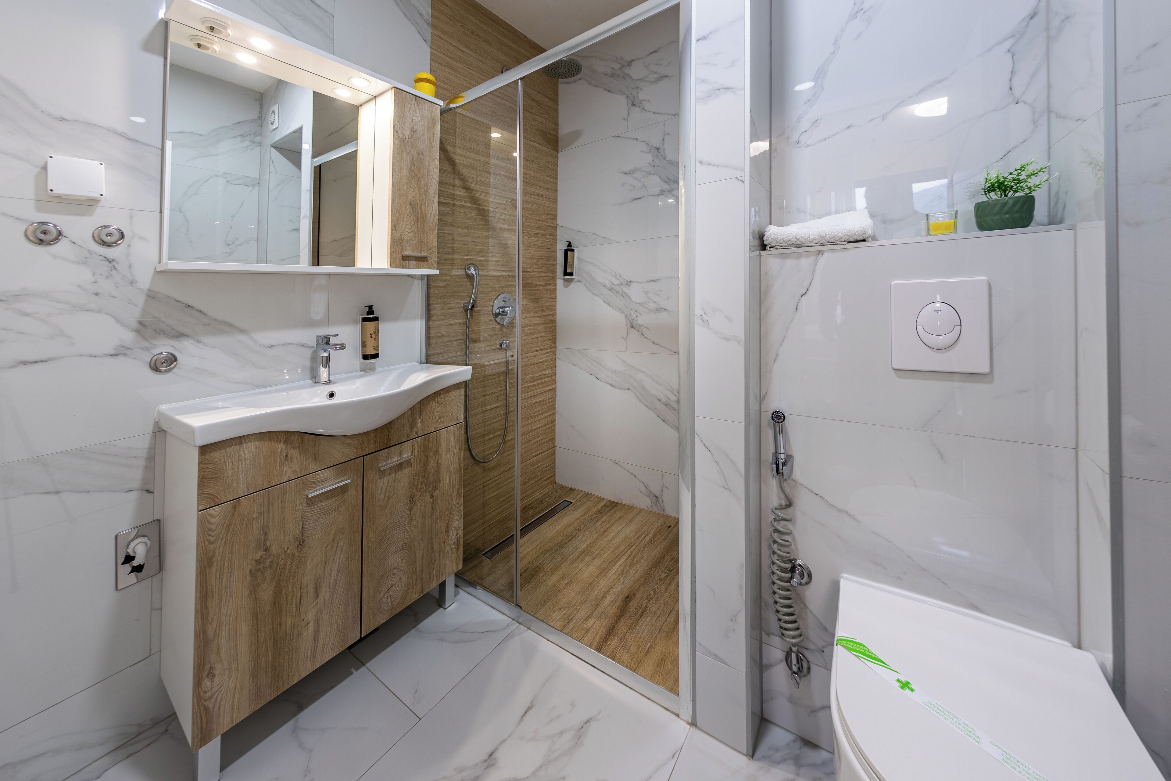 A modern bathroom with a marble floor, wooden vanity, and a glass-enclosed shower.