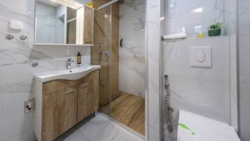 A modern bathroom with a marble floor, wooden vanity, and a glass-enclosed shower.