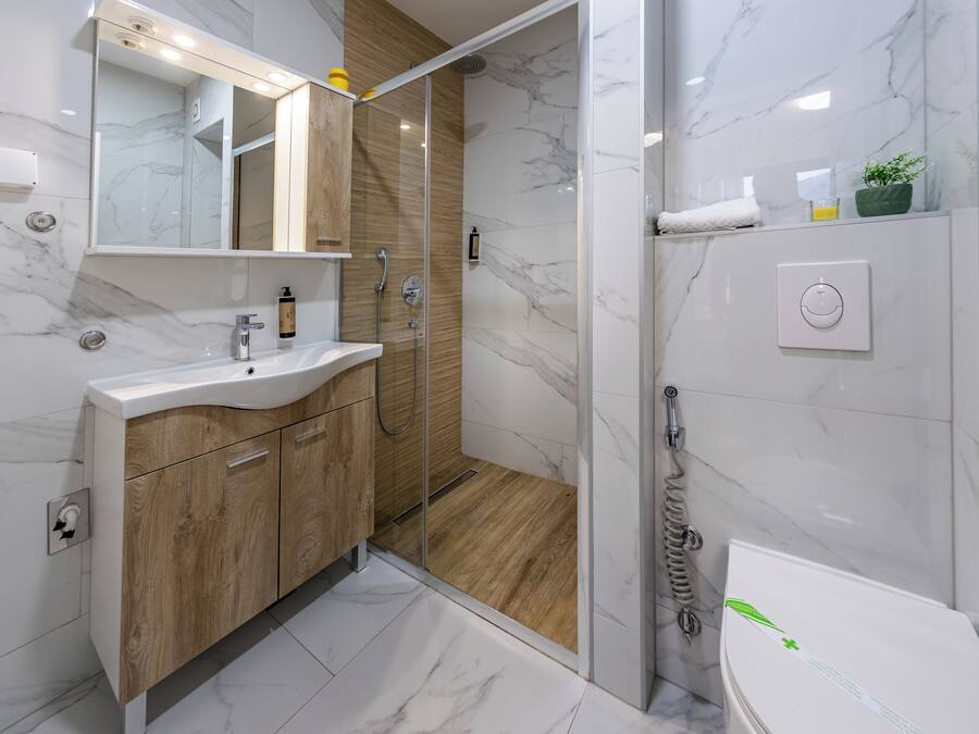 A modern bathroom with a marble floor, wooden vanity, and a glass-enclosed shower.