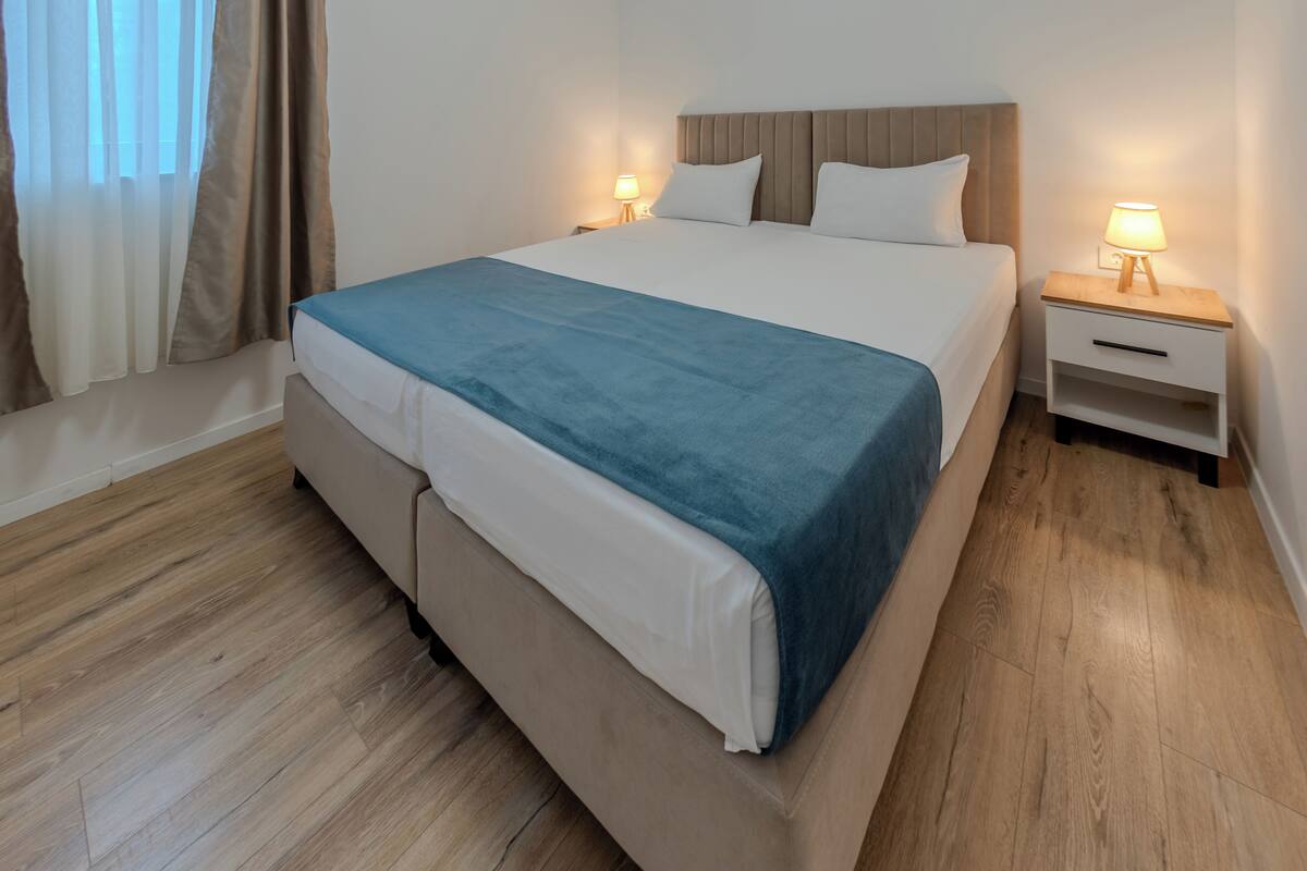 A neatly made bed with a blue blanket, a wooden headboard, and two bedside tables with lamps.