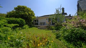 A house with a front porch, surrounded by lush greenery and flowering plants. - Carew, Bantham Beach in S. Devon (Bantham)