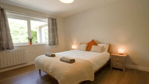 A bedroom with a bed, bedside lamps, a window with curtains, and a radiator. - Carew, Bantham Beach in S. Devon (Bantham)