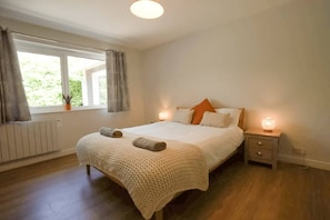 A bedroom with a bed, bedside lamps, a window with curtains, and a radiator. - Carew, Bantham Beach in S. Devon (Bantham)