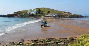 A beach with a dune, a beach buggy, and buildings on the hill.