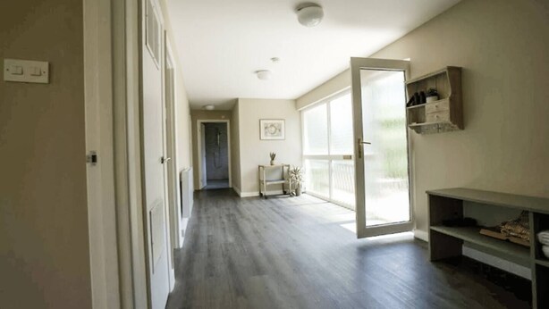 A hallway with a door leading to a room, a small table with a plant, and a shelf with items. - Carew, Bantham Beach in S. Devon (Bantham)