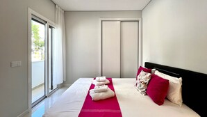 A modern hotel room with a large bed, a bright window, and a door. - PRAIA DA ROCHA MODERN by HOMING (Praia da Rocha)