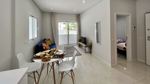 A modern living room with a dining area, a sofa, a TV, and a balcony with a view. - PRAIA DA ROCHA MODERN by HOMING (Praia da Rocha)
