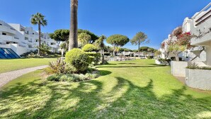 A well-maintained garden with palm trees and manicured lawns, surrounded by modern buildings with balconies. - ALBUFEIRA BALAIA GOLF VILAGE 2 WITH POOL by HOMING (Albufeira)