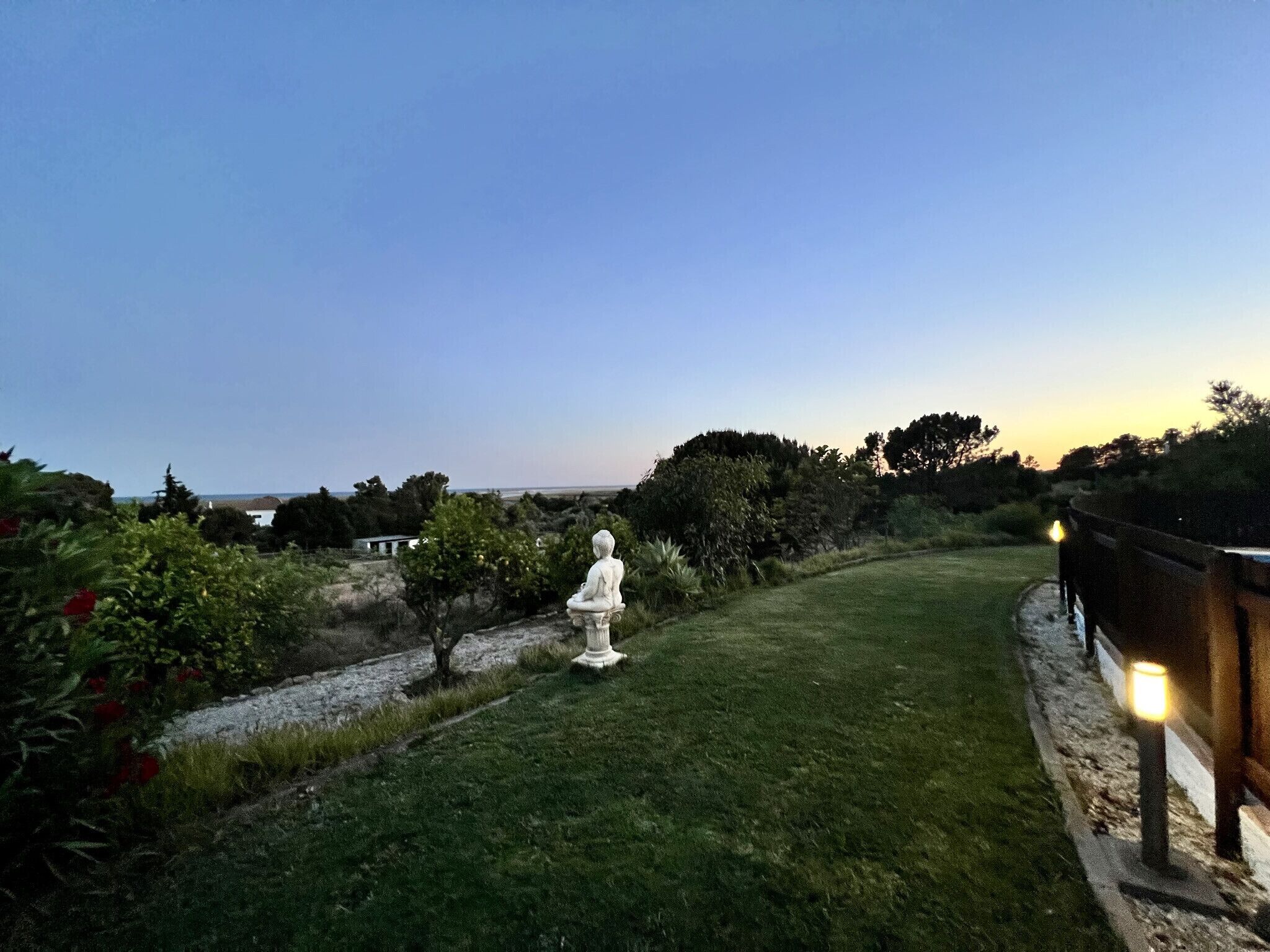 A serene outdoor garden with a statue, a pathway, and a view of the sea.