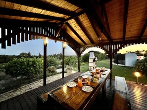Una terraza de madera al aire libre con una mesa larga dispuesta para el desayuno, con vistas a un paisaje pintoresco.