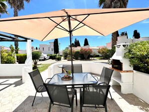 Un patio al aire libre con una mesa redonda y sillas, un paraguas grande y una barbacoa.