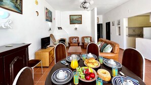 Un coin repas avec une table mise pour le petit-déjeuner, comprenant des assiettes, des couverts et une variété de fruits et de viennoiseries.