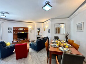 A modern living room with a TV, sofa, and dining area with a table set for breakfast. - TAVIRA PALM TREE by HOMING (Tavira)