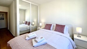 Ein Hotelzimmer mit einem großen Bett, einem Kleiderschrank, einem Nachttisch mit Lampe und einem Spiegel.