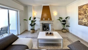 Ein Wohnzimmer mit Kamin, zwei Blumentöpfen, einem weißen Couchtisch und einem Sofa.