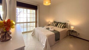 A bedroom with a bed, bedside tables, a mirror, and a window with curtains. - VILAMOURA GARDEN VIEW 2 WITH POOL by HOMING (Vilamoura)