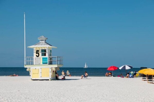 Une tour de surveillance avec le numéro 5, des parasols de plage et des personnes se détendant sur le sable.