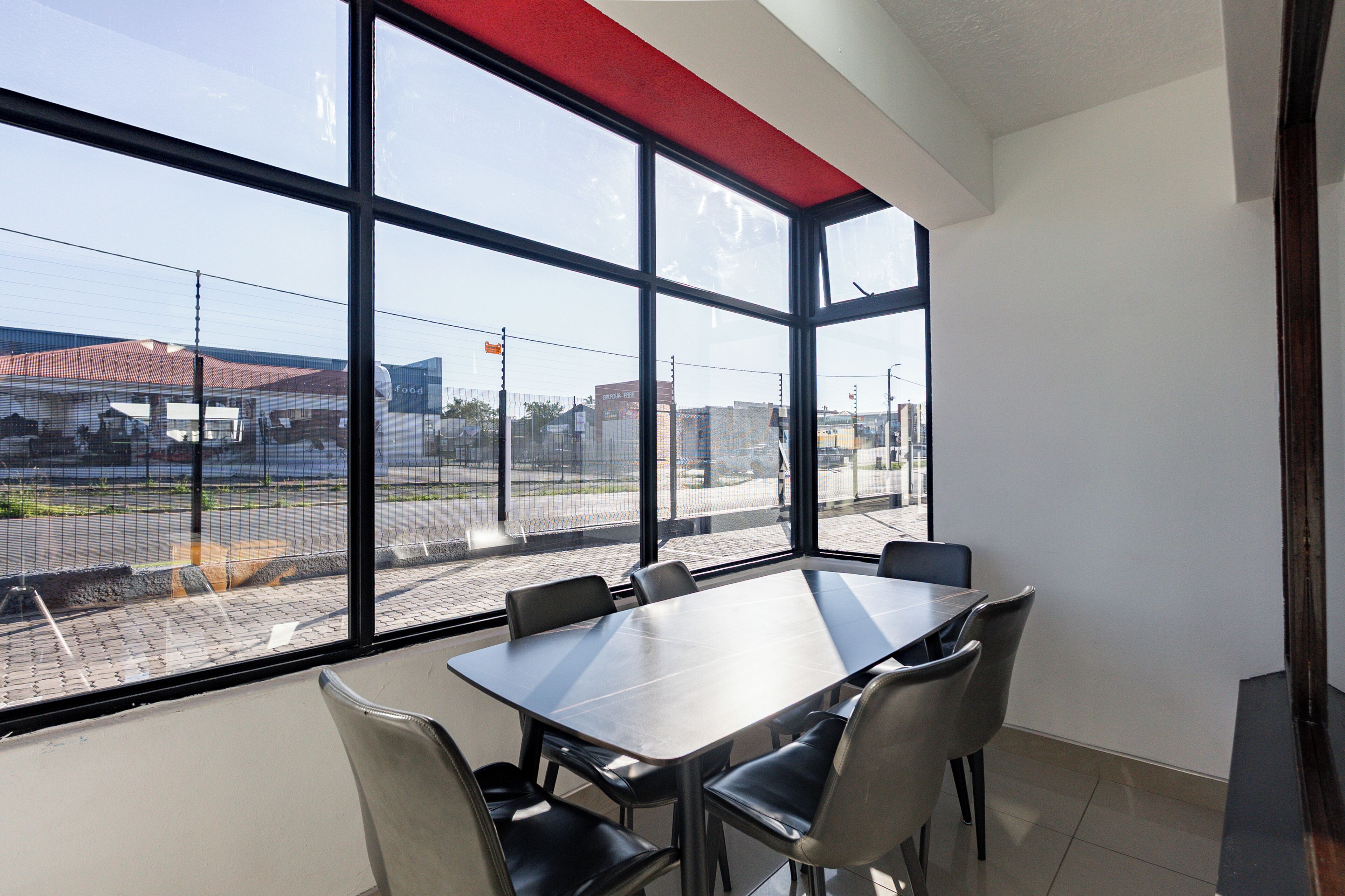 A conference room with a large table and chairs, large windows with a view of a parking lot and buildings.