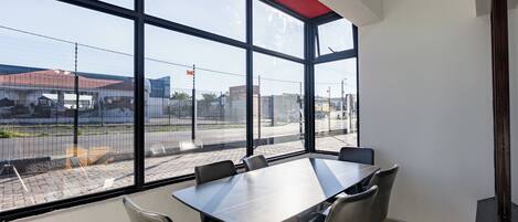 A conference room with a large table and chairs, large windows with a view of a parking lot and buildings.