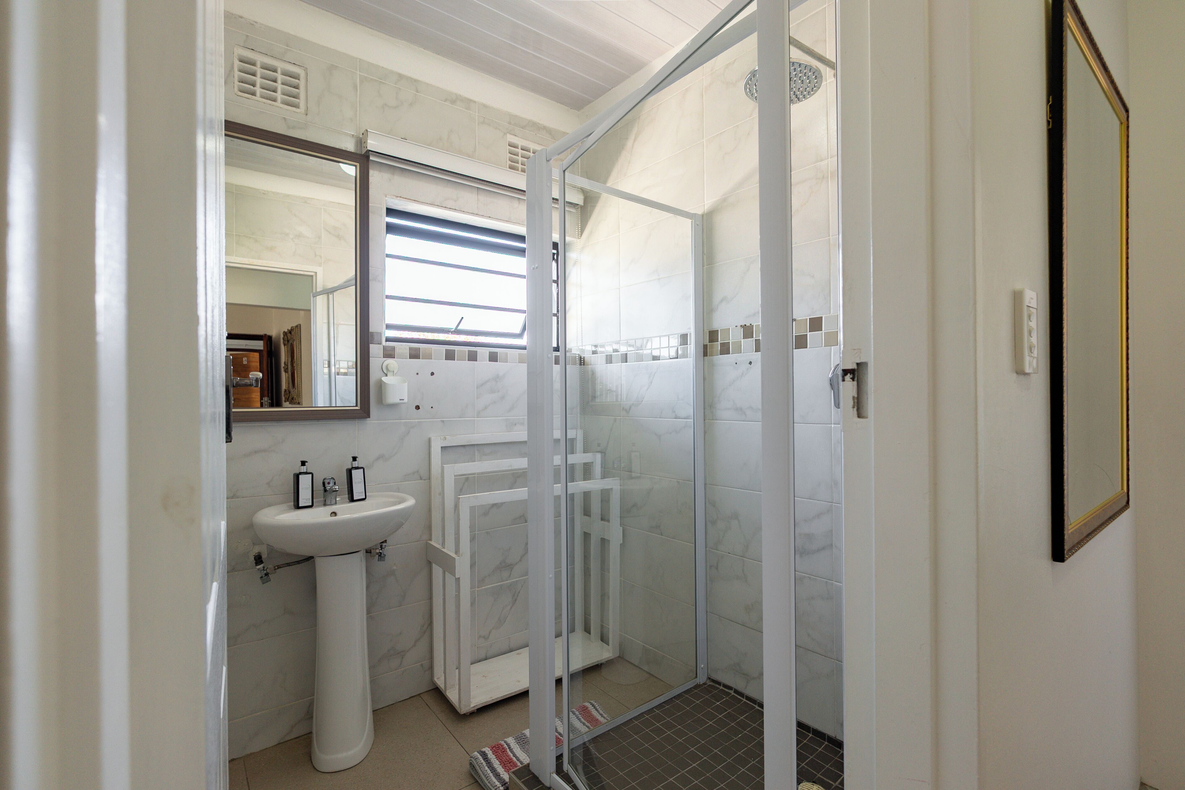 A bathroom with a pedestal sink, a glass shower enclosure, and a mirror.